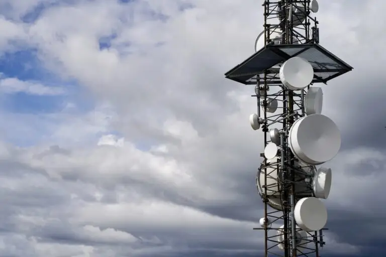 Telekomunikacijski stolp z antenami proti oblačnemu nebu.